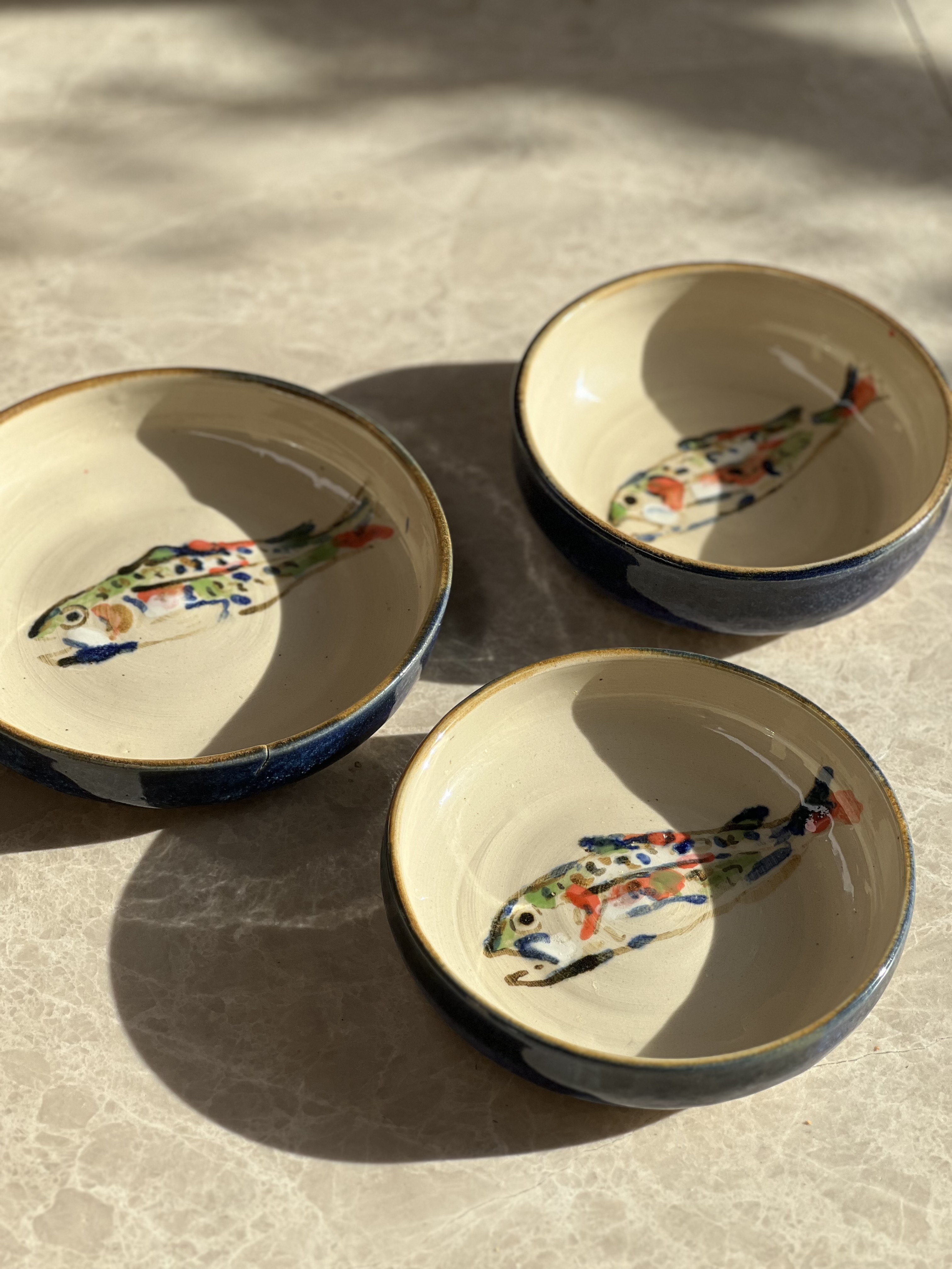 Two hand-painted fish-motif ceramic bowls on marble